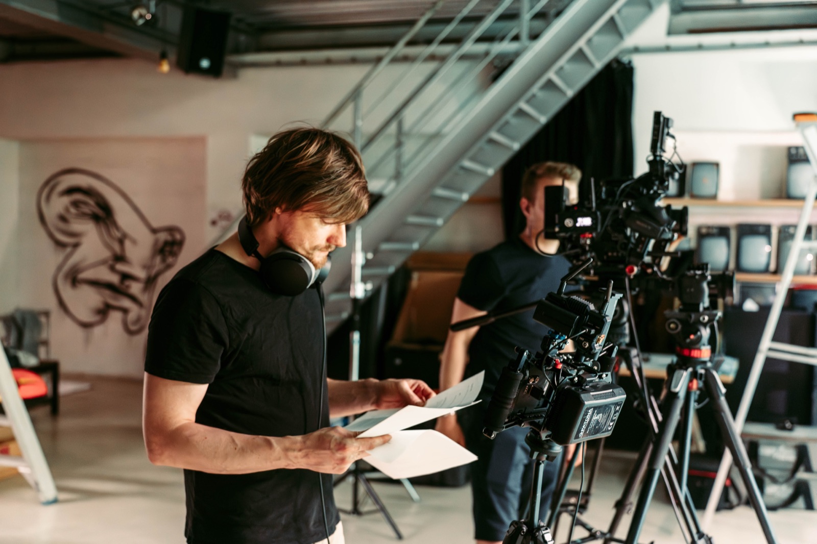 Yves Creten reading a shot list on set, with camera rigs and a crew member in the background